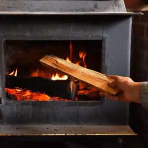 someone putting a wood log into a wood stove